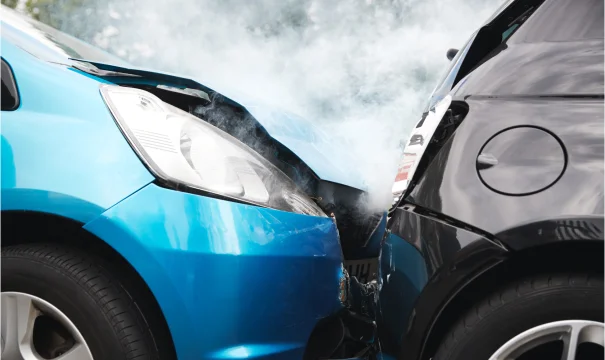 Close-up of a blue car and a black car colliding, smoke billowing from the damaged hoods after a serious accident.