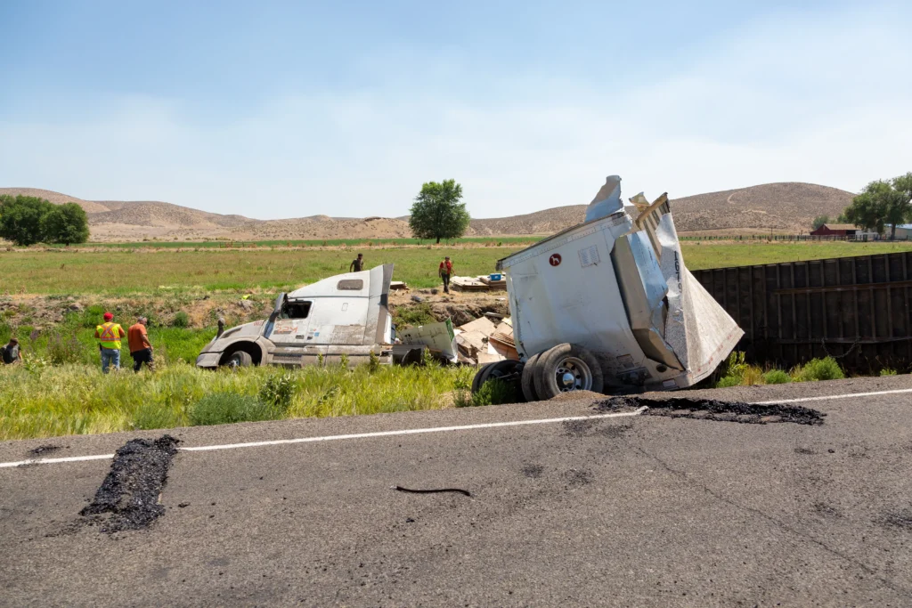 A semi-truck overturned in a ditch, with workers nearby assessing the situation