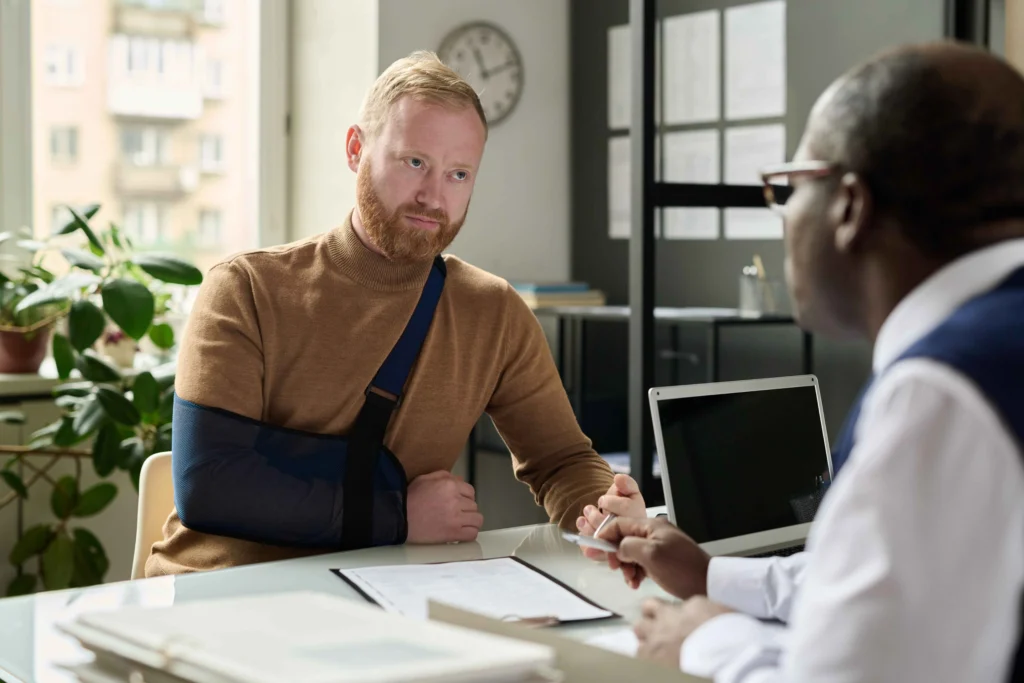 A man with a sling engages in a serious conversation with another man at a des