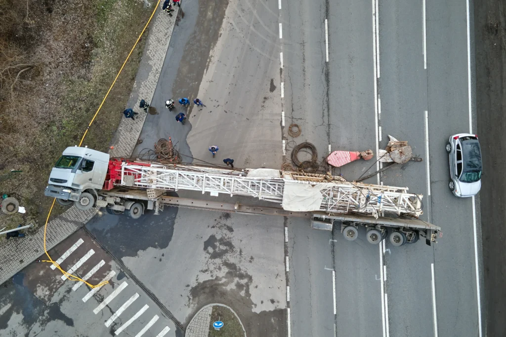 An aerial view of a construction truck blocking a road, with construction workers and equipment nearby, amidst traffic.