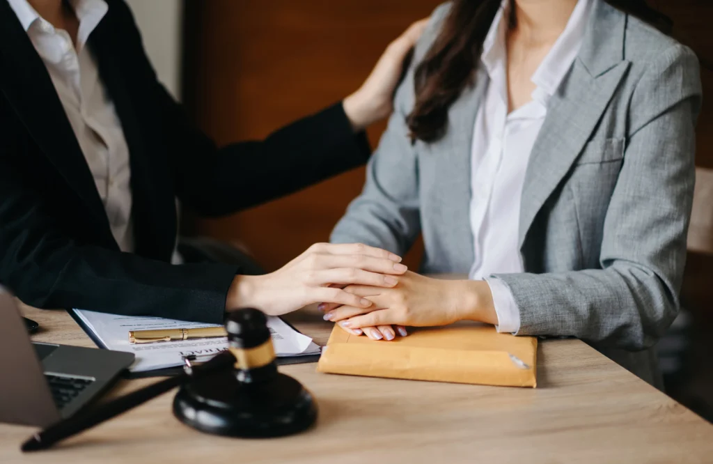 A supportive lawyer gently touches the hand of a client in a professional setting, with a gavel and documents on the table.